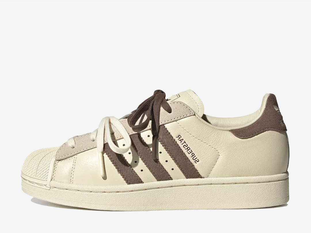 The Adidas Superstar Molly-Mae Latte reworks the classic silhouette with a clean, minimal aesthetic. Built with a leather upper, signature shell toe, and durable rubber sole, the shoe maintains its heritage design while feeling more contemporary. Finished in warm beige and cream tones with subtle branding, it delivers a neutral, versatile look suited to everyday styling.
