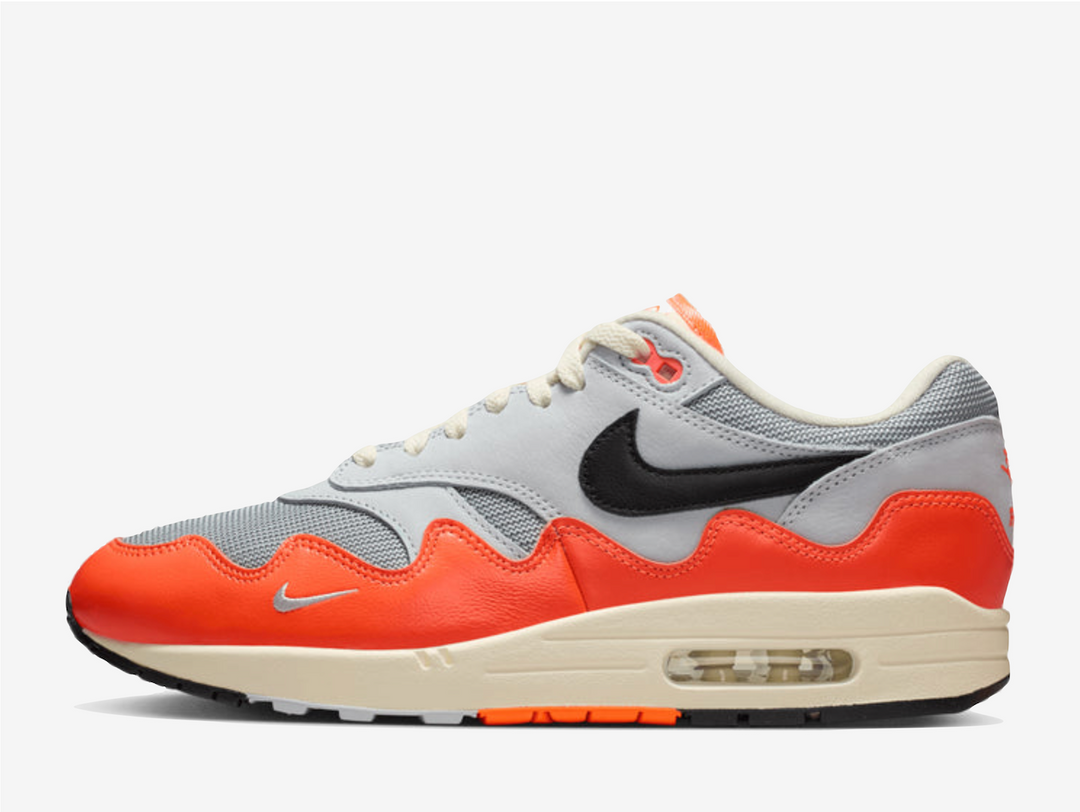 The Patta x Nike Air Max 1 “Orange Grey” reimagines a classic with the signature wave-rippled mudguard from the iconic Waves pack. Hyper Crimson accents reference Dutch national pride, while Pure Platinum and natural white tones keep the upper clean and wearable. Finished with smooth leather overlays and a gold bracelet featuring Swoosh detailing and the Surinamese flag, it blends heritage with modern streetwear style.
