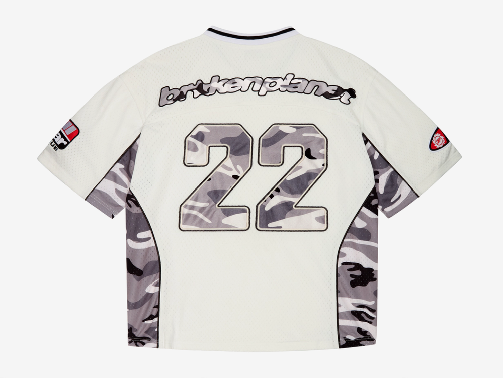 A standout piece built with a premium recycled polyester mesh construction, finished with satin camo appliqué embroidery across the chest and back for a layered, textured look. Detailed with sleeve patches, a woven label, and embroidered neck patch, combining classic sportswear references with elevated finishing throughout. Designed with a true-to-size fit for everyday wear, we recommend taking your usual size.