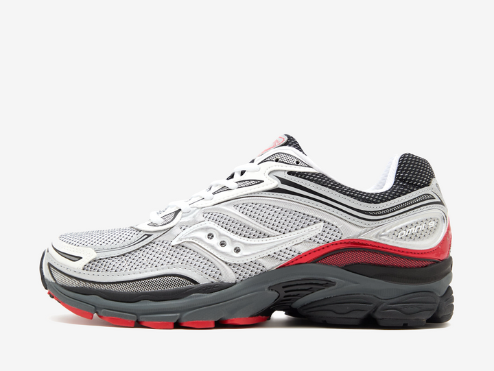The Saucony ProGrid Omni 9 Light Grey features a breathable grey mesh upper with layered silver overlays, black detailing and bold red accents across the heel and outsole. Underfoot, the chunky black midsole combines Saucony’s ProGrid cushioning with a durable rubber outsole, giving the pair a comfortable feel and distinctive retro-running look.