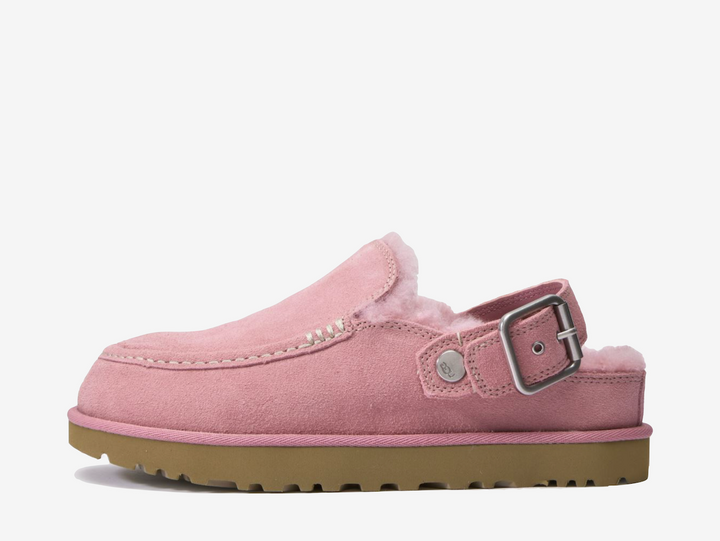 The UGG Goldenstar Evelina Clog Pink features a soft suede upper in a pastel pink finish, complete with decorative stitching and an adjustable heel strap. A plush interior and lightweight EVA outsole provide cushioning and everyday comfort.