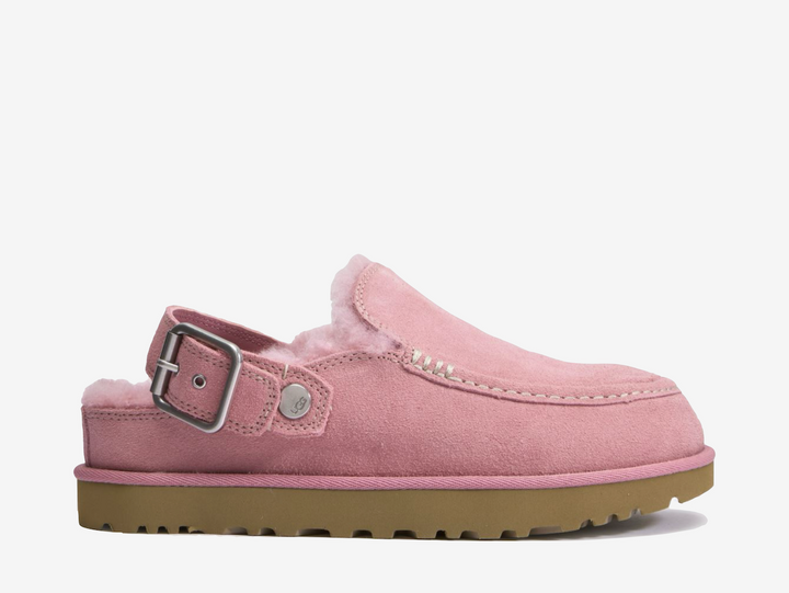 The UGG Goldenstar Evelina Clog Pink features a soft suede upper in a pastel pink finish, complete with decorative stitching and an adjustable heel strap. A plush interior and lightweight EVA outsole provide cushioning and everyday comfort.