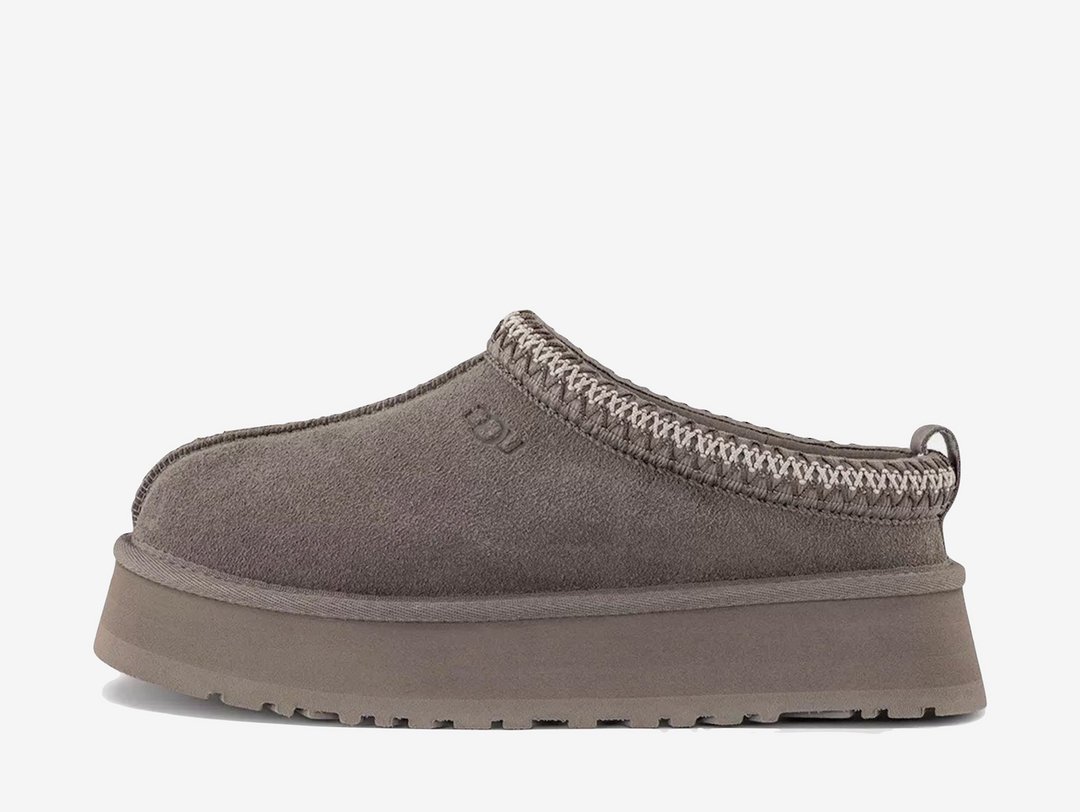 The UGG Tazz Slipper Smoke Plume Sea Salt combines soft grey and neutral tones across its suede upper and signature collar detailing. A plush lining and chunky platform sole complete the pair with warmth, comfort and a distinctive elevated shape.
